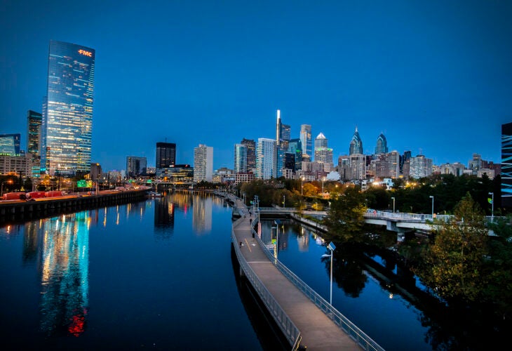 Philadelphia skyline at dusk with skyscrapers reflecting on the Schuylkill River and Schuykill Banks boardwalk.